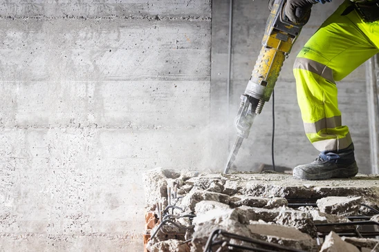 Chantier de construction en ext&eacute;rieur, ouvrier en v&ecirc;tements haute visibilit&eacute; jaune fluorescent utilisant un marteau-piqueur pneumatique pour d&eacute;molir du b&eacute;ton arm&eacute;