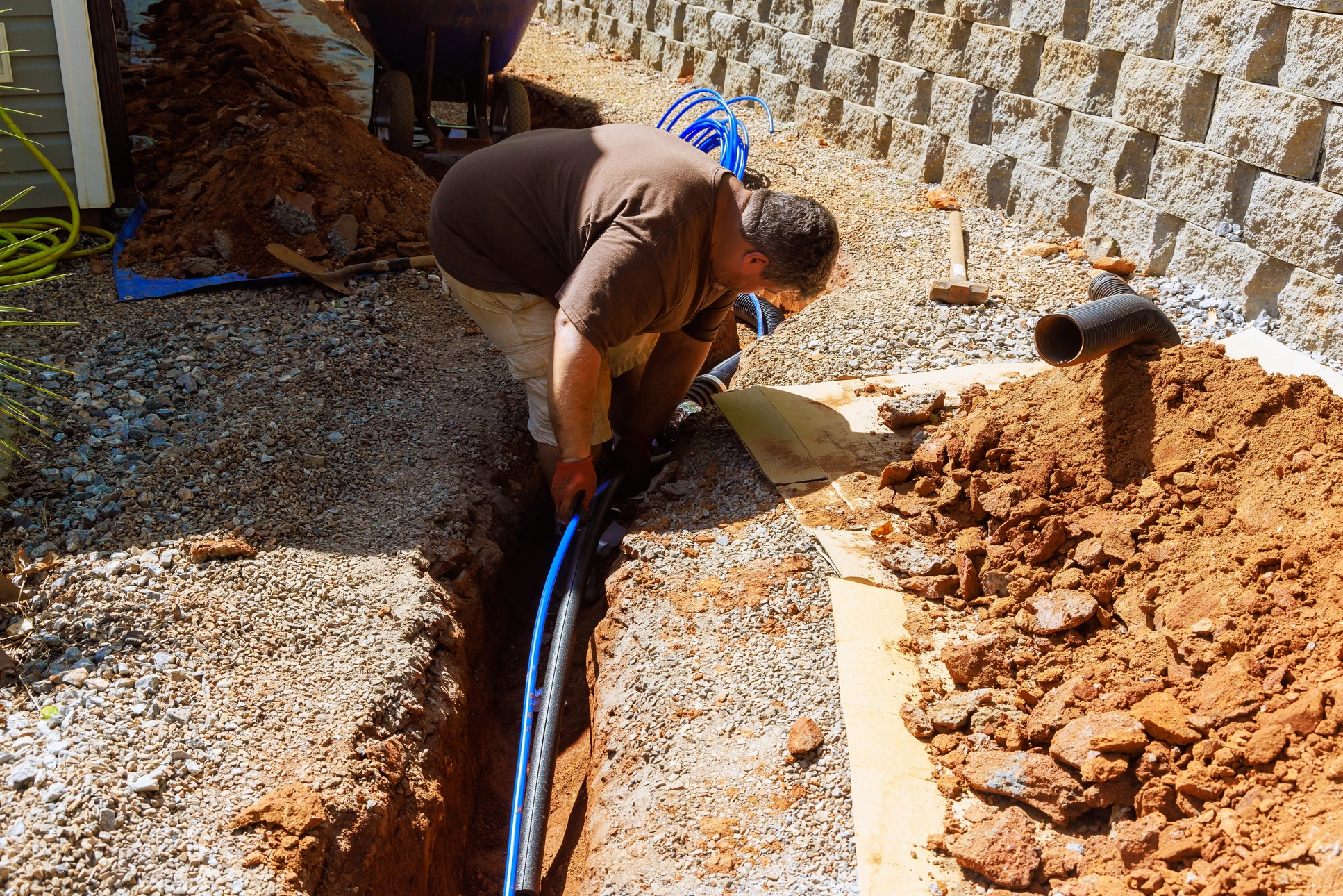 Ouvrier en combinaison installant une canalisation souterraine dans une tranchée sur chantier résidentiel