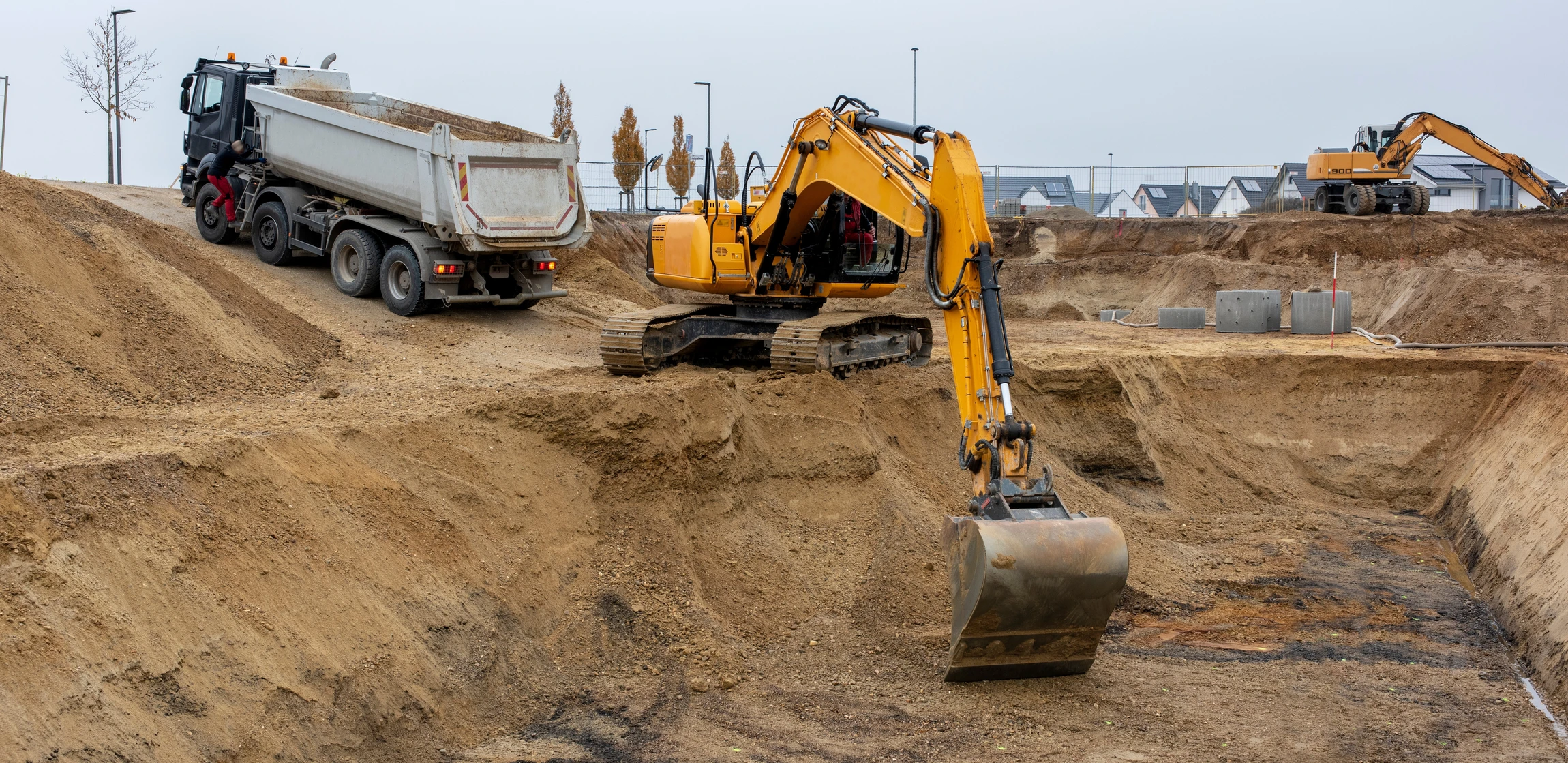 Chantier de terrassement en extérieur avec pelleteuse hydraulique sur chenilles jaune en action, camion-benne blanc pour transport de matériaux, excavation de terre et tranchées
