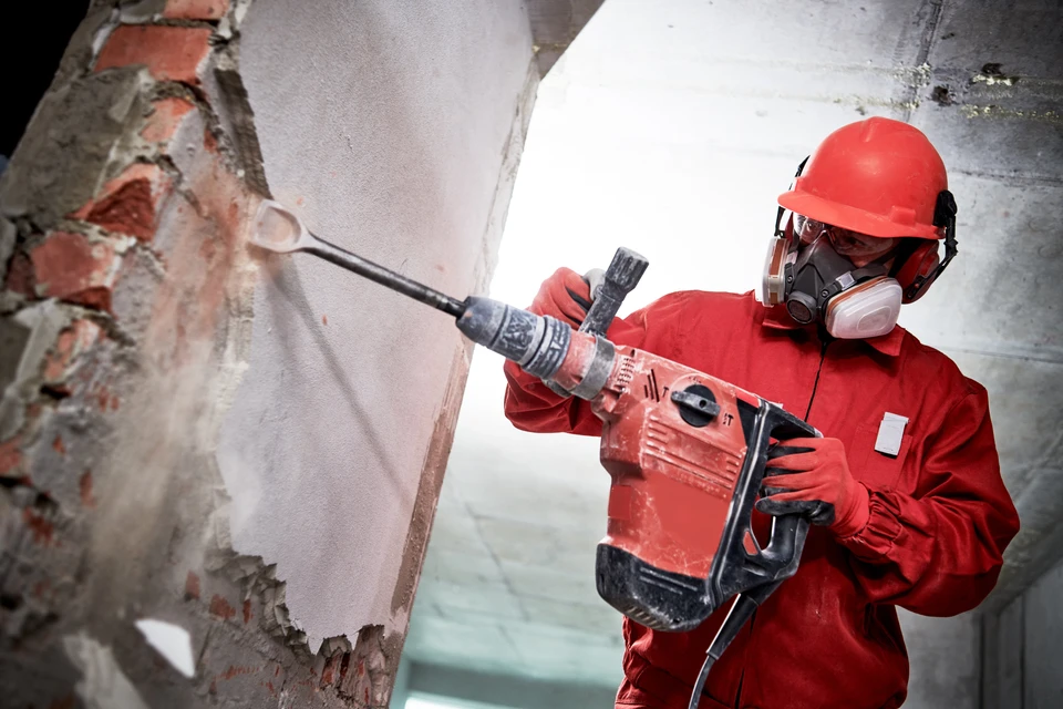 Ouvrier en combinaison rouge de protection utilisant un marteau-piqueur pneumatique pour démolir un mur en béton à l'intérieur d'un bâtiment